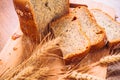 Close slice of fresh bread with poppy seeds and wheat ears on wooden background