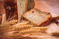 Close slice of fresh bread with poppy seeds and wheat ears on wooden background