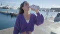 Close slomo of girl in purple top by harbor drinking out of bottle