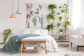 Close to nature bright bedroom interior with a bed covered with white sheets and marine blanket. Green plants on shelves next to t