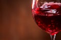 Close-up of the abstract splashing of the red wine in the fragile wineglass on the brown wooden background.