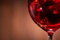 Close-up of the abstract splashing of the red wine in the fragile wineglass on the brown wooden background. Royalty Free Stock Photo