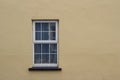 Close up abstract view of a white window surrounded by an smooth yellow solid wall texture Royalty Free Stock Photo