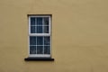 Close up abstract view of a white window surrounded by an smooth yellow solid wall texture Royalty Free Stock Photo