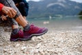 Close up of active woman putting on hiking boots on shore of mountain lake. Senior tourists enjoying nature during early Royalty Free Stock Photo