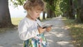 CLOSE UP: Adorable baby girl watching fun cartoons on her mother`s cell phone during family walk down tree promenade. Royalty Free Stock Photo