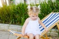 Close up Adorable blondy baby girl in dress or toddler child sitting and relaxing on a sunbed or a deckchair in the city park recr Royalty Free Stock Photo