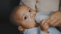 Close up adorable dark skin baby drinking his milk from the bottle in mothers hands Royalty Free Stock Photo