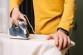 Close up of adult man with watch on hand iron white shirt on pressboard using electric flatiron. Male doing housework.