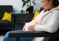 Close-up of an adult pregnant woman smiling, touching her belly, feeling baby movements, sitting relaxed on sofa indoors Royalty Free Stock Photo
