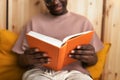 Close up of African American man hands holding book. Black man relaxing at home, reading a book. Focus on hands.