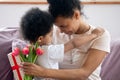 Close up african american mother holding flowers, bouquet and gift. Royalty Free Stock Photo