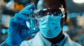 Close up of an African American scientist holding a glass vial with blue liquid, glass in focus. Wearing a medical mask and gloves Royalty Free Stock Photo