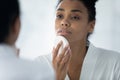 African woman reflecting in mirror holding facial sponge cleanses face