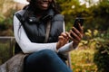 Close up of afro woman using mobile phone while sitting outdoors Royalty Free Stock Photo