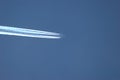 Close up of an airliner flying through the dark blue sky with multiple contrails stretching out behind it.