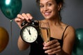 Close-up of an alarm clock and flute of champagne in the hands of blurred smiling beautiful woman, isolated over gray background