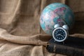 Close up of alarm clock on the old holy bible with blurred world globe on vintage linen sackcloth background