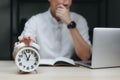 Close up alarm clock with young Businessman using laptop analysis marketing plan and come up with new ideas in the night. Business Royalty Free Stock Photo