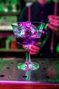 Close up of alcoholic cocktail, beverage, drink, prepared by professional barman in multicolored neon light