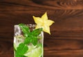 Close-up of an alcoholic mojito drink with fresh lime, mint, ice and decorative carambola on a dark wooden background. Copy space. Royalty Free Stock Photo