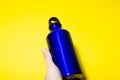 Close-up of aluminium thermo eco water bottle in hand, classic blue of color, isolated on yellow background.