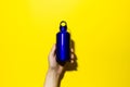 Close-up of aluminium thermo eco water bottle in hand, classic blue of color, isolated on yellow background.