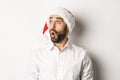 Close-up of amazed bearded man in santa hat, looking left with surprised face, christmas promo offer, standing over