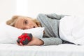 Close-up of amazed blonde girl holding small gift box while lying in bed, looking at camera Royalty Free Stock Photo
