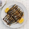 Malaga cuisine grilled sardines served with lemon on white plate on wooden table