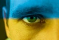 Close up of an angry male green eye. Blue and yellow colors on his face as symbol of patriotism and inviolability of Ukraine