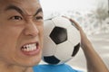 Close up of angry young man holding a soccer ball on his shoulder Royalty Free Stock Photo