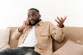 Close-up of an annoyed African American young man sitting on a couch talking on a cell phone. Angry black young man Royalty Free Stock Photo