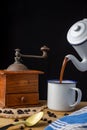 Close-up of antique coffee maker serving coffee in white cup with old coffee grinder, coffee beans and spoon on wooden table and b Royalty Free Stock Photo