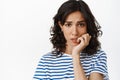 Close up of anxious brunette girl, biting fingernails and looking embarrassed at camera, feel nervous and scared