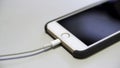 Close up of the apple iphone with the charging cable lying on the white table. Media. Process of charging of a modern