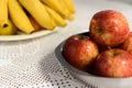 Close-up of apples in a metal bowl in the background, a bunch of bananas on a plate.