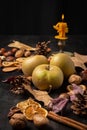 Close-up of apples, nuts, oranges, cinnamon, burning candle and autumn leaves, on black background,