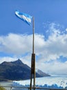 Close up of Argentine flag waving under blue sky and background of Perito Moreno glacier. Patagonian mountains. Landscapes and Royalty Free Stock Photo