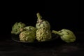 Close-up of artichokes on black plate on wooden table, with selective focus, black background, Royalty Free Stock Photo