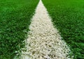 Close-up of artificial turf. Blurred legs of soccer players in the background. The white line on the artificial soccer field. The