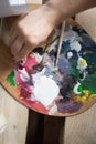 Close-up of the artist& x27;s hand with a wooden palette paint from a tube is squeezed out for mixing. Creative workshop for Royalty Free Stock Photo