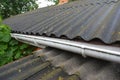 A close-up of an asbestos roof with a plastic roof gutter. An old corrugated asbestos roof