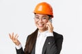 Close-up of asian businesswoman manage enterprise, engineer in safety helmet and suit having phone conversation, calling Royalty Free Stock Photo