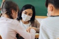 Close-up of Asian female teacher wearing face mask in school building tutoring a primary student children. Elementary Royalty Free Stock Photo