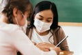 Close-up of Asian female teacher wearing a face mask in school building tutoring a primary student girl. Elementary Royalty Free Stock Photo