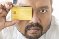 Close-up of Asian man holding yellow gold credit card in his hand close the right eye isolated on white background. Concept of Royalty Free Stock Photo