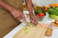 Close-up Asian man's hand using kitchen knife cut gherkin into round shapes, prepare them for cooking in evening