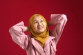 Close up of Asian muslim teenage girl wearing yellow hijab looking up and thinking, hands behind head and smiling for having good