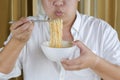 Asian plus size man in white shirt using silver chopstick to eating instant noodles with blowing on hot noodle Royalty Free Stock Photo
